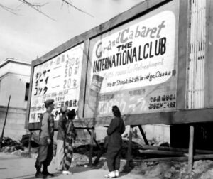 People standing beneath a large cabaret opening advertisement in Shinsaibashi in November 1945.